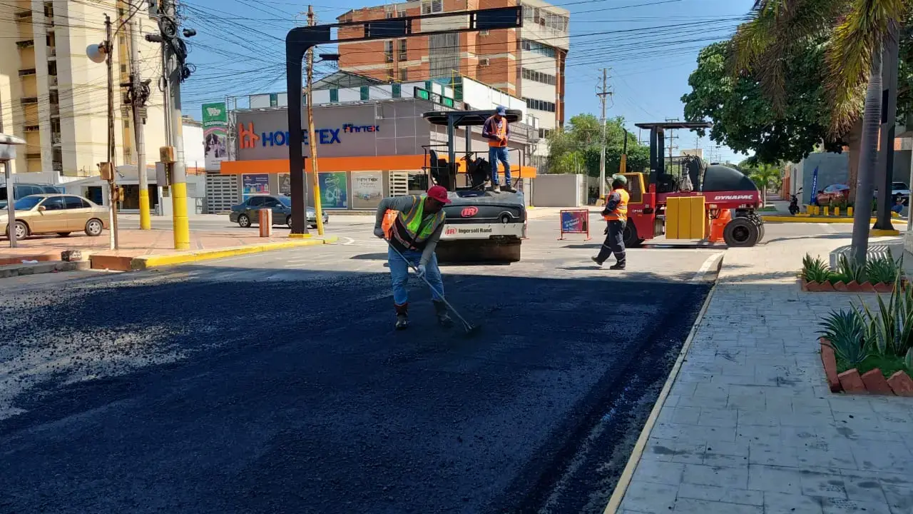 Trabajador con casco y chaleco extendiendo mezcla asfáltica en la vía